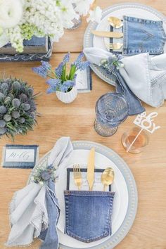 a wooden table topped with plates and napkins covered in blue denim cloth, silverware