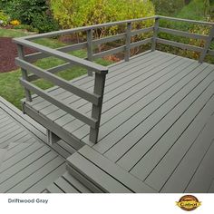 a wooden deck with metal railings in front of some bushes and flowers on the other side