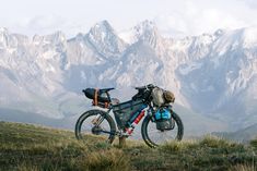 a bicycle parked on top of a grass covered hill with mountains in the back ground