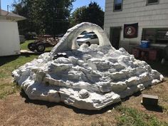 a large rock formation sitting in the middle of a yard next to a house and car