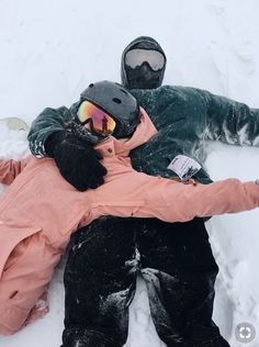 two people laying on the snow with skis and goggles attached to their backs