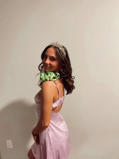 a woman in a pink dress with a green flower on her neck and wearing a tiara