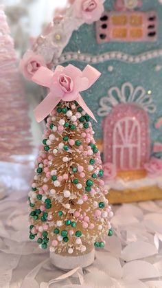 a small christmas tree with pink and green beads on it's top, next to a gingerbread house