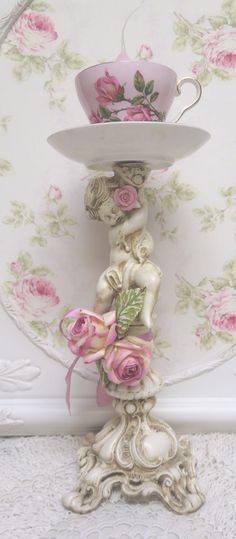 there is a cup and saucer sitting on top of a stand with roses around it