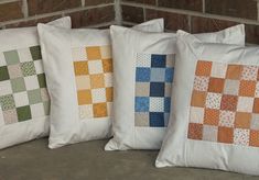 four pillows are lined up against a brick wall, each with different colored squares on them