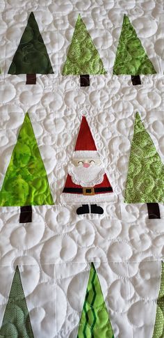 a quilted christmas tree with santa clause on it's face and green trees in the background