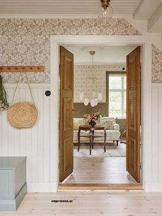 an open door leading to a living room with floral wallpaper on the walls and wood flooring