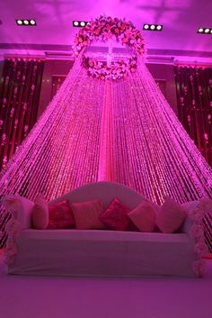 a couch with pink pillows in front of a purple curtain and lights on the ceiling