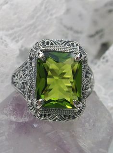 Simulated Green Peridot Ring Autumn Design #D200 Inspired by Victorian era designs, this lovely filigree reproduction has been recreated in sterling silver. This flawless 5 carat simulated Green Peridot gemstone is 12mm x10mm in size. The ring sits 17mm (11/16") North to South on the finger. The inside of the band is etched 925 for sterling silver. Notice the intricate and detailed design of the antique silver filigree setting all the way down the band. This is an exquisite rendition of an antiq Classic Peridot Jewelry With Accent Stones, Elegant Green Filigree Ring For Wedding, Elegant Green Filigree Ring With Gemstone, Elegant Rectangular Peridot Rings, Classic Green Filigree Ring With Gemstone, Green Filigree Ring With Intricate Design For Wedding, Elegant Filigree Ring With May Birthstone, Elegant Filigree Ring As May Birthstone Gift, Elegant Rectangular Peridot Jewelry