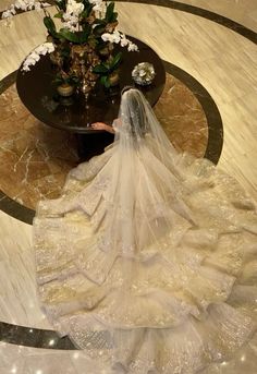 a woman in a wedding dress is sitting on the floor next to a vase with flowers