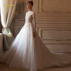 a woman in a white wedding dress standing next to a window with curtains on it