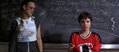 two people standing in front of a blackboard with writing on it and one person pointing at the camera