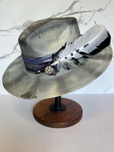 This is a gorgeous stiff brim painted fedora accented with purple, silver, and black colors. This hat is a size large with an elastic inner band for the most comfortable fit. Please see size chart in the pictures. Adjustable Fedora With Feather Trim For Kentucky Derby, Adjustable Wide Brim Fedora With Feather Trim, Adjustable Wide-brim Fedora With Feather Trim, Adjustable Wide Brim Purple Fedora, Adjustable High Crown Silver Hat, Adjustable Silver High Crown Hat, Adjustable Purple Brimmed Fedora, Adjustable Purple Fedora With Short Brim, Silver Hat With Adjustable Fit And Short Brim