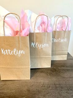 three brown paper bags with white writing on them sitting on a wooden table next to each other