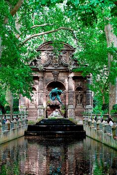 a fountain in the middle of a park surrounded by trees