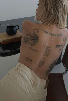 a woman with tattoos on her back sitting in front of a table and coffee cup