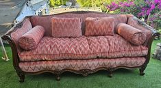 an old fashioned couch sitting on top of a green grass covered field with purple flowers in the background