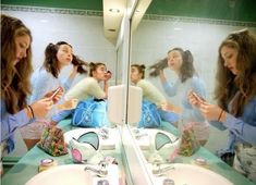 the girls are looking at their cell phones in the mirror while they brush their teeth