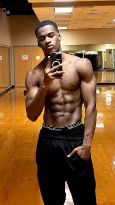 a shirtless man taking a selfie with his cell phone in an empty gym