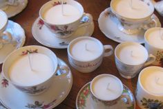 tea cups and saucers with lit candles in them sitting on a wooden table top