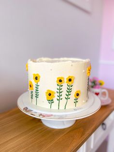 a white cake with yellow flowers on it sitting on top of a wooden countertop