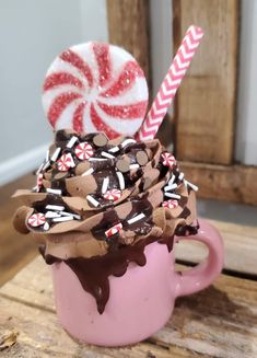 a pink cup filled with chocolate and candy canes on top of a wooden table