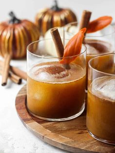 three glasses filled with drinks on top of a wooden tray next to small pumpkins