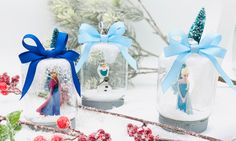 three snow globes with frozen princess figures in them and blue bows on the top