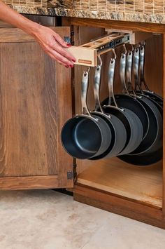 a kitchen cabinet with pots and pans hanging from it's pull out rack