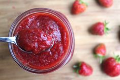 a spoon full of strawberry jam sitting on top of a wooden table next to strawberries