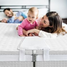 a woman holding a baby laying on top of a bed with two other people in the background