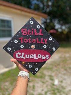 someone holding up a graduation cap that says still totally clueless