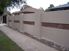 a concrete fence with some rocks on the side and grass in front of it next to a sidewalk