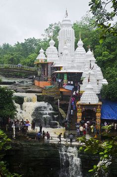 a group of people standing in front of a waterfall next to a white building with pillars