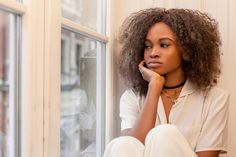 a woman sitting on the window sill with her hand under her chin looking out