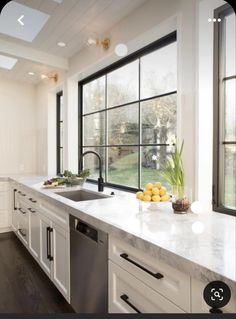 a large kitchen with white cabinets and marble counter tops, along with black framed windows