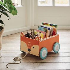 a wooden toy cart filled with books on top of a hard wood floor next to a potted plant