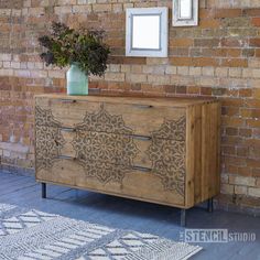 a wooden dresser with an intricate design on the front and sides, against a brick wall