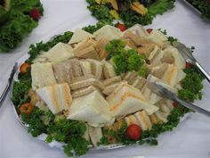 a platter filled with sandwiches and salads on top of a white table cloth