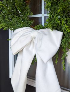 a white bow tied to the side of a door with greenery on it's front