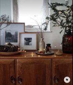 there is a wooden cabinet with candles and pictures on the top, along with pine cones