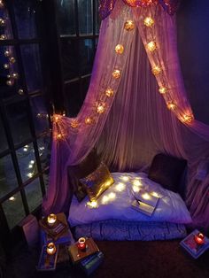 a bed covered in lights next to a window with a purple curtain and pillows on it