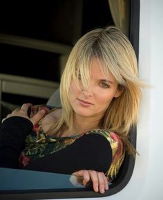 a woman leaning out the window of a vehicle with her hand on her shoulder and looking at the camera