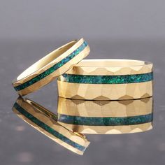 two gold rings with green and blue opal inlays sitting on top of each other