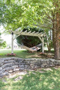 a hammock hanging from a tree in a yard with stone wall and grass