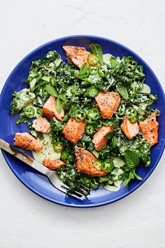 a blue plate topped with salad and salmon on top of green lettuce next to a fork