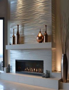 a modern fireplace in a living room with white tiles and silver vases on the mantel