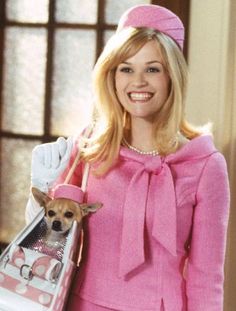 a woman in pink dress holding a small dog on her shoulder and smiling at the camera