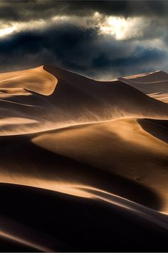 the sun shines through the clouds over sand dunes