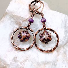 Purple glass flowers floating inside twisted copper rings make these Boho dangle earrings extra special. Copper rings frame the flower beads that have shades of purple, lavender and a Picasso finish.  Lightweight and versatile, these cute earrings will add a pop of color and sophistication to your look.  Custom ear wire style choice at checkout. Hypoallergenic ear wires (nickel and lead free).  Free gift packaging included. Earrings are carded and in an organza bag. Artisan glass beads produced Artsy Copper Drop Earrings, Artsy Nickel-free Copper Earrings, Artsy Copper Jewelry With Matching Earrings, Copper Jewelry With Matching Round Bead Earrings, Unique Metal Flower Jewelry, Artsy Electroformed Jewelry For Gifts, Unique Flower Shaped Metal Jewelry, Nickel-free Copper Artsy Jewelry, Unique Flower-shaped Metal Jewelry